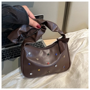 Detail einer braunen Ledertasche mit bunten Strasssteinen und gerafftem Griff