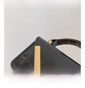 Detail of golden hardware and chain strap on a black crocodile pattern crossbody bag