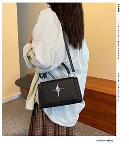 Detail of black pebbled leather crossbody bag with silver star logo and woven handle