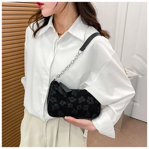Detail of black underarm bag with embossed floral texture and silver chain strap