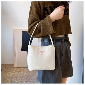 Close-up of cream canvas handbag featuring pink embroidered lettering and slim handles