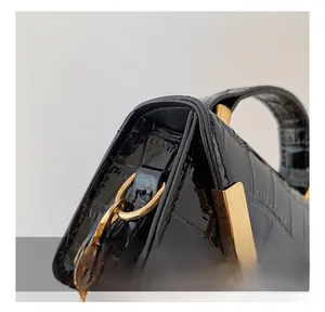 Detailed close-up of golden metal hooks and hardware on black crocodile pattern bag