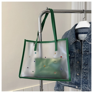 Close-up of clear PVC tote bag featuring colorful faux gems and green leather trim