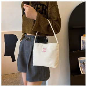 Detail of minimalist cream nylon shoulder bag with pink embroidery text on a model
