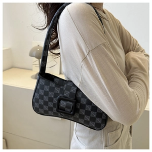 Detail of checkered shoulder bag with black buckle worn by a model in a minimalist room