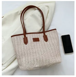 Top view of a large straw tote bag with brown leather handles and a mobile phone comparison