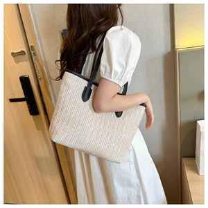 Close-up of beige straw tote bag with black leather handles showing woven texture