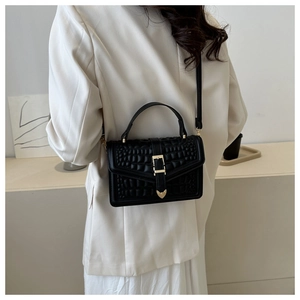 Close-up of black stone pattern crossbody bag with gold buckle on a white blazer