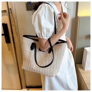 Close-up of a large straw tote bag with black leather trim worn by a model in a white dress