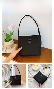 Detail of black nylon shoulder bag with pink letter embroidery on a minimalist wooden table