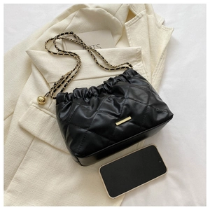 Détail d'un sac bandoulière noir matelassé avec chaîne dorée et breloque en métal