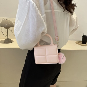 Pink quilted crossbody bag with plush pompom keychain worn by a model in a cafe setting