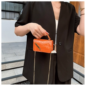 Detail of orange crocodile pattern mini bag with gold chain and metal hardware on flap