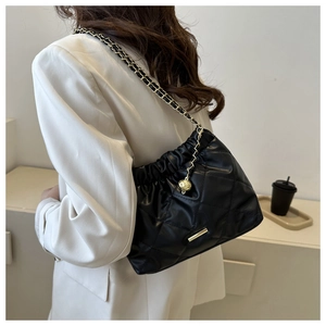 Detail of black quilted shoulder bag featuring gold chain strap and spherical charm
