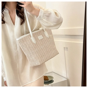 Detail of a large straw tote bag with white leather handles and a woven texture design