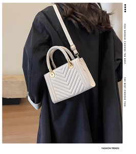 Detailed view of a white quilted handbag featuring a woven handle and gold hardware detail