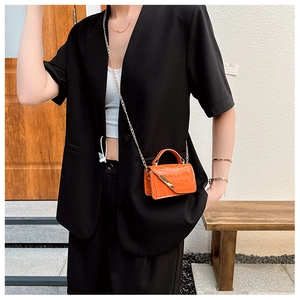 Close-up of orange crocodile pattern crossbody bag with gold chain on model in black suit