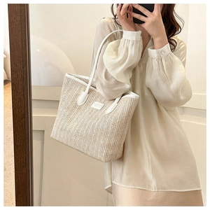 Detail of large woven straw tote bag with white leather trim and brand plate detail