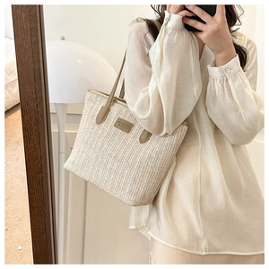 Detail of a beige woven tote bag with slim khaki leather handles and brand logo patch