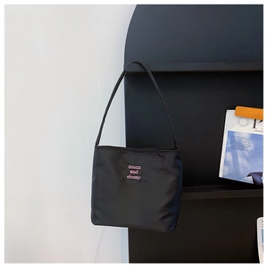 Detail of pink embroidered text on a black nylon shoulder bag with a sleek finish