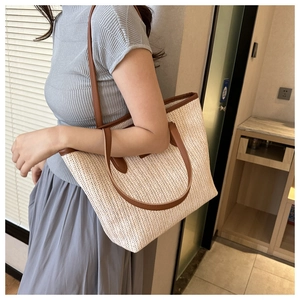 Close-up of large straw tote bag with brown leather handles worn by a model