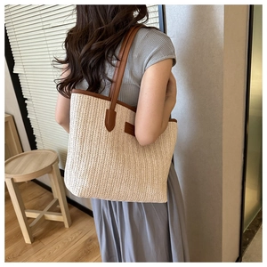 Large capacity woven straw tote bag with brown leather handles worn by a model in soft light