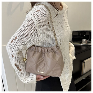 Détail du sac seau matelassé beige avec chaîne dorée et cordon de serrage porté par un mannequin