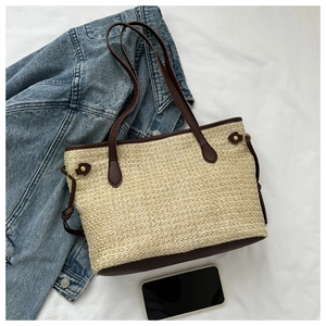 Close-up of beige woven tote bag with brown leather handles on white linen background