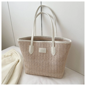 Detail of a beige straw tote bag with white leather straps and stitched logo patch
