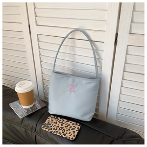 Close-up of light blue nylon tote bag featuring pink embroidery on a black leather sofa