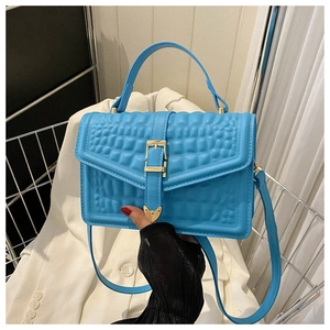 Detail of bright blue faux crocodile leather bag with golden buckle and adjustable strap