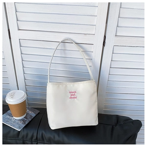 Detailed view of white nylon shoulder bag with pink embroidery on a black leather bench