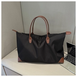 Detail of a large black nylon tote bag with brown leather handles and reinforced corners