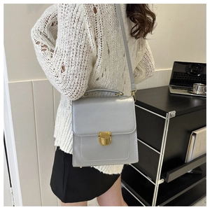 Close-up of a light grey PU leather crossbody bag with a round gold metal push-lock buckle