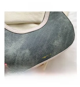 Detail of washed blue denim half-moon bag with beige leather trim and printed text