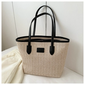Detail of woven straw tote bag texture with black leather handle and minimalist brand tag