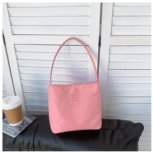 Detail of pink nylon shoulder bag with embossed letters on black leather surface