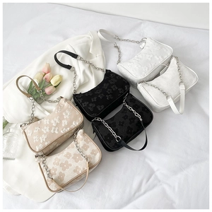 Flat lay of pleated floral crossbody bags in black, white, and tan with chain straps