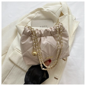Détail d'un sac matelassé beige avec bandoulière en chaîne dorée et boule décorative