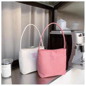 Detail of embroidered logo on pink and white nylon tote bags in a cafe setting
