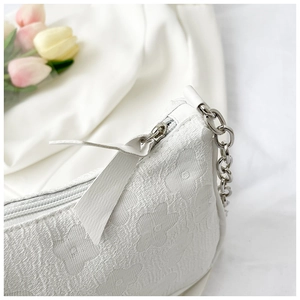 Close-up of white floral lace fabric texture with silver metal zipper and chain strap