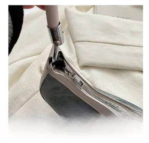 Detailed close-up of the smooth silver metal zipper and cream leather piping on grey bag