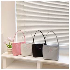 Detailed view of four colorful nylon tote bags with brand embroidery on minimalist shelf
