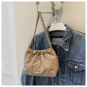 Détail du sac à chaîne matelassé beige avec plaque logo dorée sur fond en jean bleu