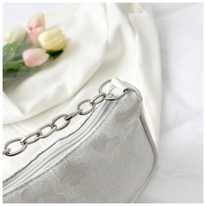 Detail of white jacquard fabric featuring butterfly floral patterns and silver metal chain