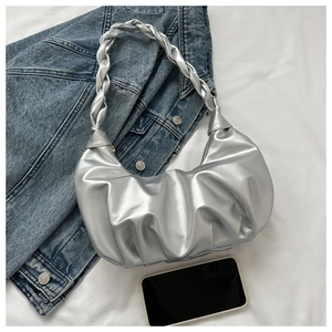 Close-up of silver pleated dumpling bag with woven handle next to denim jacket