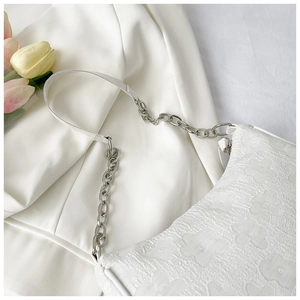 Detail of white pleated shoulder bag with floral texture and silver chain strap