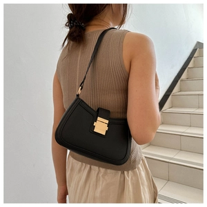 Détail d'un sac sous le bras en cuir noir vintage avec boucle dorée porté par un modèle