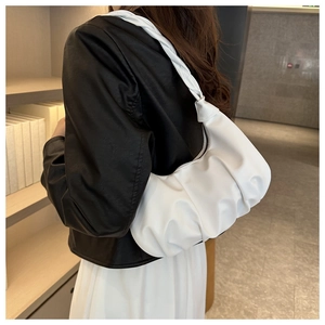 Close-up of white ruched cloud bag with woven knot strap worn on female shoulder
