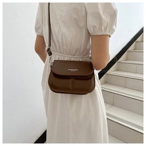 Detail of dark brown leather crossbody bag with pleated base and fashion slogan